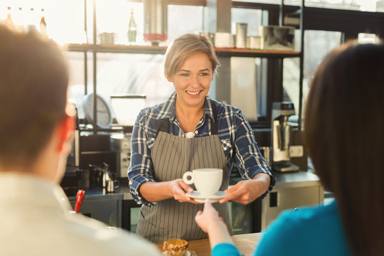 Experienced smiling barista making coffee to customers