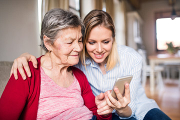 Elderly grandmother and adult granddaughter with smartphone at home.