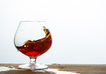 Glass of brandy or cognac splash on the wooden and white background with copy space