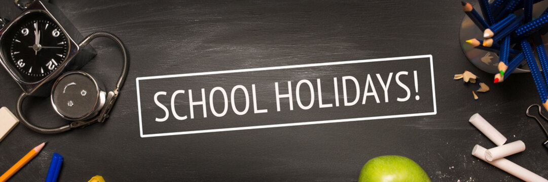 school supplies, alarm, pencils, apple on black chalkboard top view, school's out, inscription school holidays. long banner