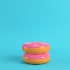 Two donuts with pink glaze on bright blue background in pastel colors