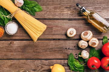 Pasta ingredients - tomatoes, olive oil, garlic, italian herbs, fresh basil, salt and spaghetti on a wooden background with copy space, horizontal, top view