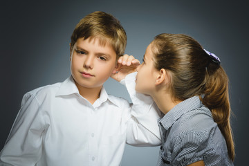 Teenage girl whispering in ear of boy on gray background. Communication concept