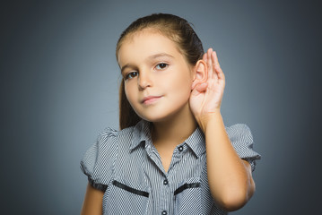 girl listens. child hearing something, hand to ear gesture on grey background.