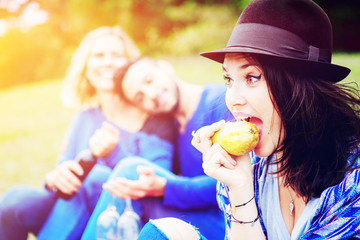 young woman eating a pear and having picnic with friends