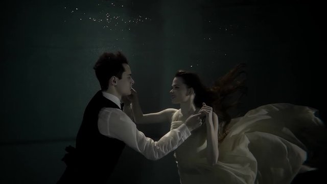 Woman diving into the water wearing white dress to her man. They are holding hands and looking at each other. Beautiful love story.