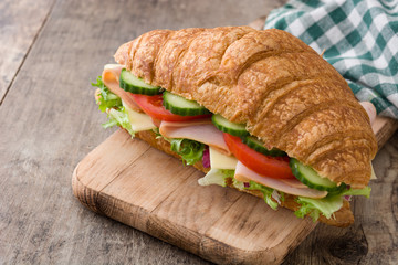 Croissant sandwich with cheese, ham and vegetables on wooden table