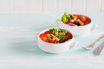 Vedan Chickpeas Salad with chia seeds, black quinoa, broccoli, tomatoes, red onion, spinach and nuts in white dishes on old light blue concrete background Clean eating, superfood, detox food concept