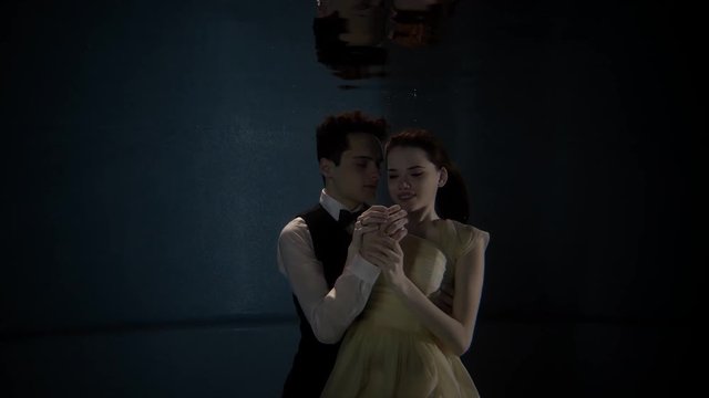 Portrait of a man and woman hugging under the water. Lovely lovers spending time underwater wearing suit and white dress.