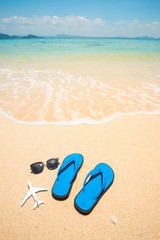 Fototapeta na wymiar Airplane, flip flop sandals and sunglasses on the beach with blue turquoise sea in background