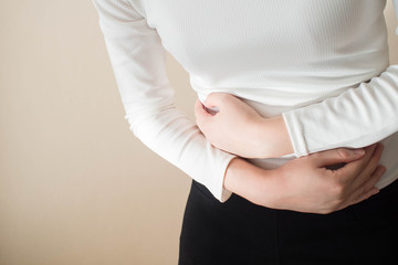 Young female suffering form stomach ache on gray background w/ copy space. Causes of abdominal pain...