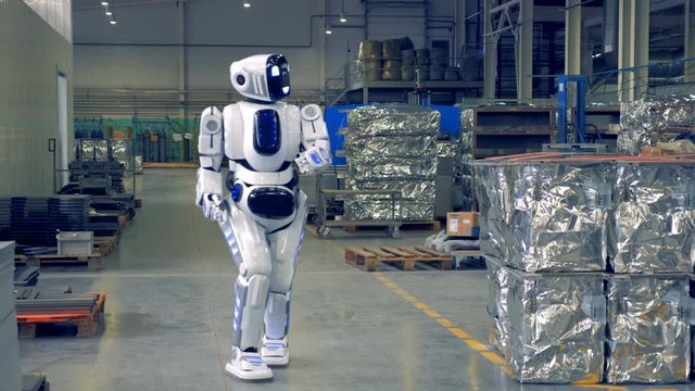 Modern robot walks in a production floor, smiling into camera.