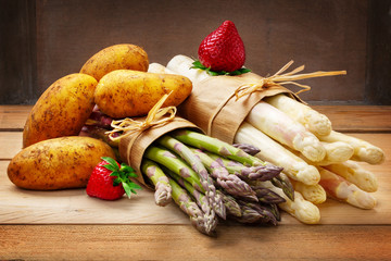 Asparagus, strawberries and potatoes on wooden board
