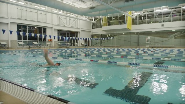 Slow motion panning shot of girl swimming freestyle in swimming pool / Provo, Utah, United States