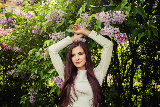Young woman with lilac flowers outdoors. Cheerful smiling brunette girl fashion model with long healthy hair