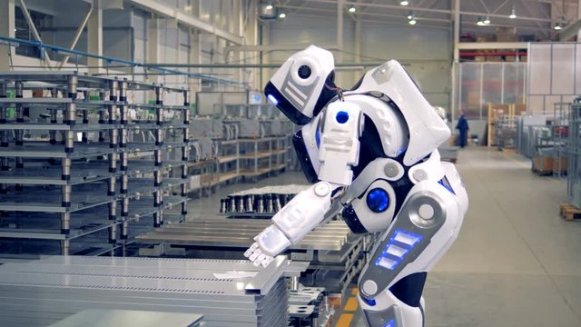 A cyborg, modern robot takes a metal sheet, then carries it.