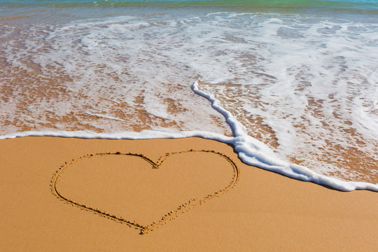 Picture of the heart on wet beach sand with the turquoise sea on background