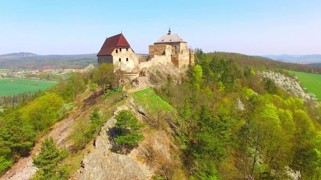 Drone flight around Tocnik Castle in blooming orchard. A royal chateau of Wenceslas IV from the 14th century, adjusted in the Renaissance and the Baroque styles. Famous Czech monument from above. 