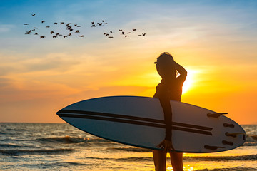 Silhouette of woman holding surfboard standing disappoint in the edge of sea wave, looking forward...