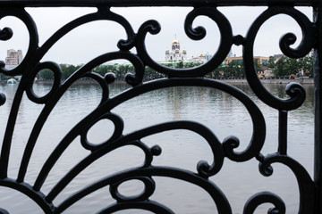 Black cast ornate lattice of city embankment fence of Yekaterinburg with view of the Temple on Blood through it.
