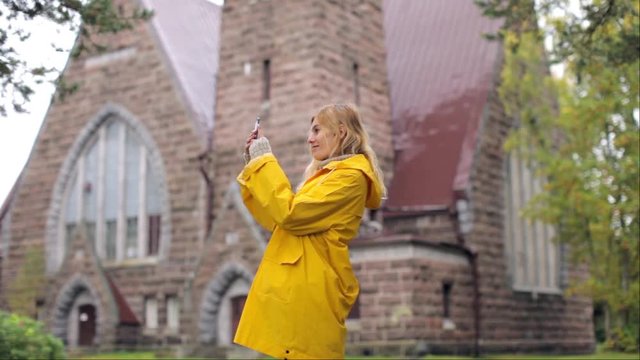 a girl in a yellow raincoat pictures on the phone near an old church