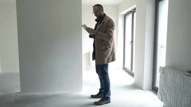 Young man, architect checking project on tablet at new home

