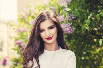 Fototapeta premium Healthy smiling woman with long hair and makeup on lilac flowers background outdoors