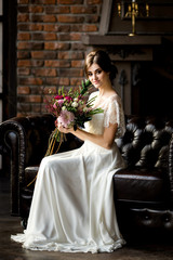 Bride in white dress sitting on chair indoors in dark studio