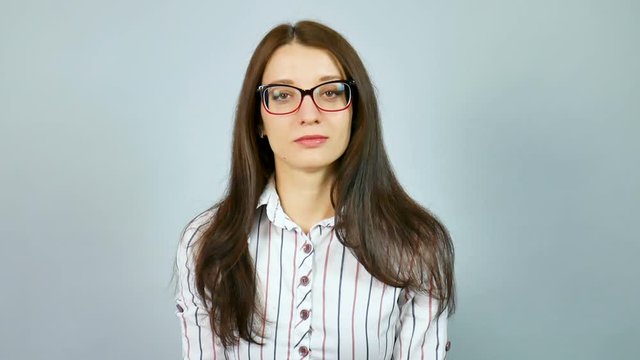 Serious Young Girl in White Shirt with Red and Blue Stripes Looking at the Camera Over Her Eyeglasses in Studio on Grey Background.