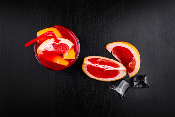Blood orange gin and tonic cocktail served with slices of orange and ice in a glass on black background