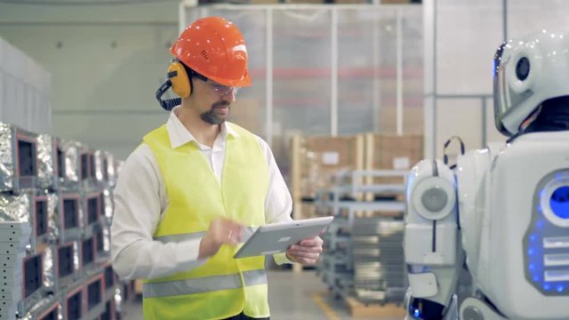 A worker talks to a robot at a warehouse.