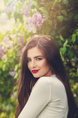 Fototapeta premium Cute young woman in blossom lilac flowers park outdoor