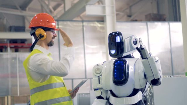 Human factory worker and an android give each other a hi-five at a factory facility.