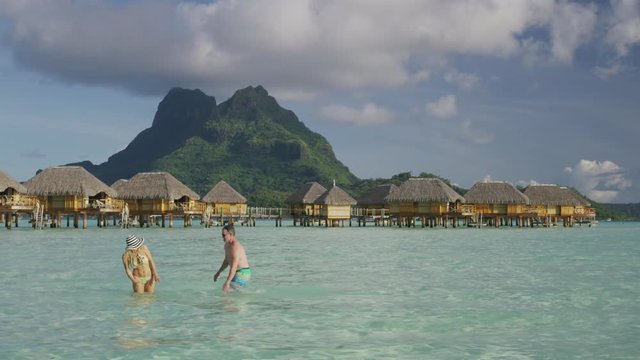 Playful couple splashing in ocean near bungalows in Tahiti / Bora Bora, French Polynesia