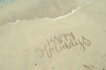 HAPPY HOLIDAYS hand lettered in sand on beach