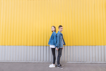 Portrait of a young couple at full height against a background of a yellow wall. A couple of hipsters in denim jackets poses against the background of the wall