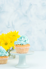 Cupcake with blue cream decoration on vintage stand and bouquet of yellow chrysanthemum in glasses vase.