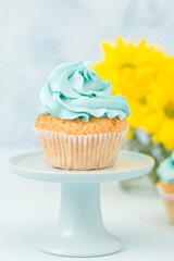 Cupcake with blue cream decoration on vintage stand and bouquet of yellow chrysanthemum in glasses vase.