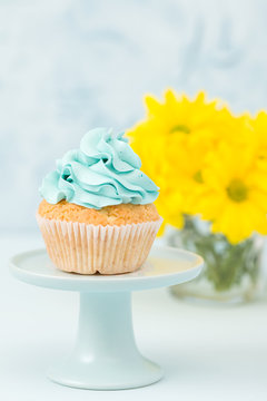 Cupcake with blue cream decoration on vintage stand and bouquet of yellow chrysanthemum in glasses vase.