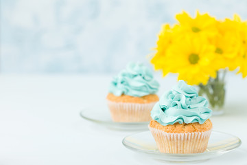 Cupcake with sweet blue cream decoration on sauser and bouquet of yellow chrysanthemum in glasses cup.
