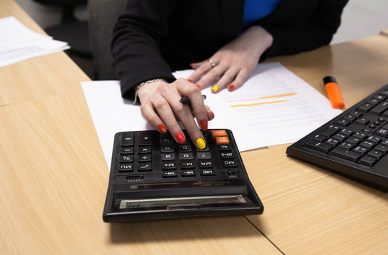 Photo of hands holding the pen and pressing the calculator buttons above the documents