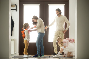 Happy family everyday preparations, caring parents getting kids with backpacks ready for first day at school standing at house hall together, boy son and girl daughter dressing in the morning at home - Powered by Adobe