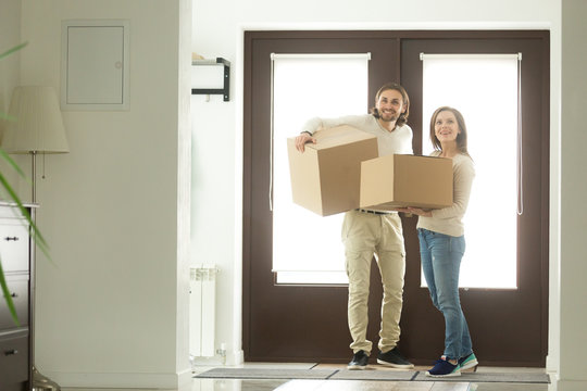 Excited young couple carrying boxes moving into new home concept, happy married family holding belongings arriving entering big own bought or rented house, buying real estate, mortgage and relocation