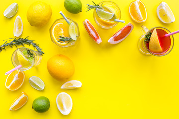 Concept of alcoholic cocktail with fruits. Glass with beverage near oranges, grapefruit, lime and rosemary on yellow background top view copy space
