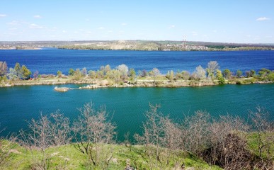 A view of the lake with turquoise water and a river with dark blue water from a hill. They share a thin strip of land on which people like to rest.