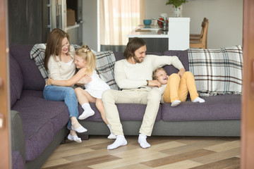 Cheerful parents playing with kids on sofa laughing together at home, mom and dad having fun...