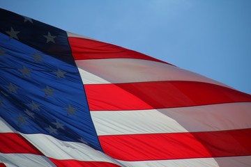 Fototapeta na wymiar American Flag Waving Against Blue Sky Backlit by Morning Sun