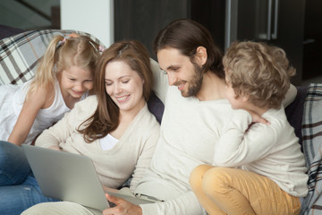 Fototapeta na wymiar Smiling parents with kids using laptop on sofa, happy family with children son daughter having fun with computer doing online shopping or watching funny video together sitting on couch at home
