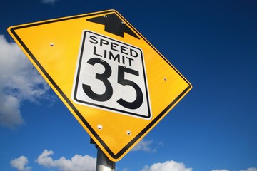 Looking Up at Speed Limit 35 Mph with Black Lettering on White Rectangle Surrounded by Yellow Diamond with Arrow Pointing Up Sign against Blue Sky with Scattered Clouds in the Afternoon Frame Left