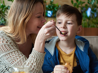 Caucasian Mom and son having good time at a cafe. Mother is doing facetious feeding.